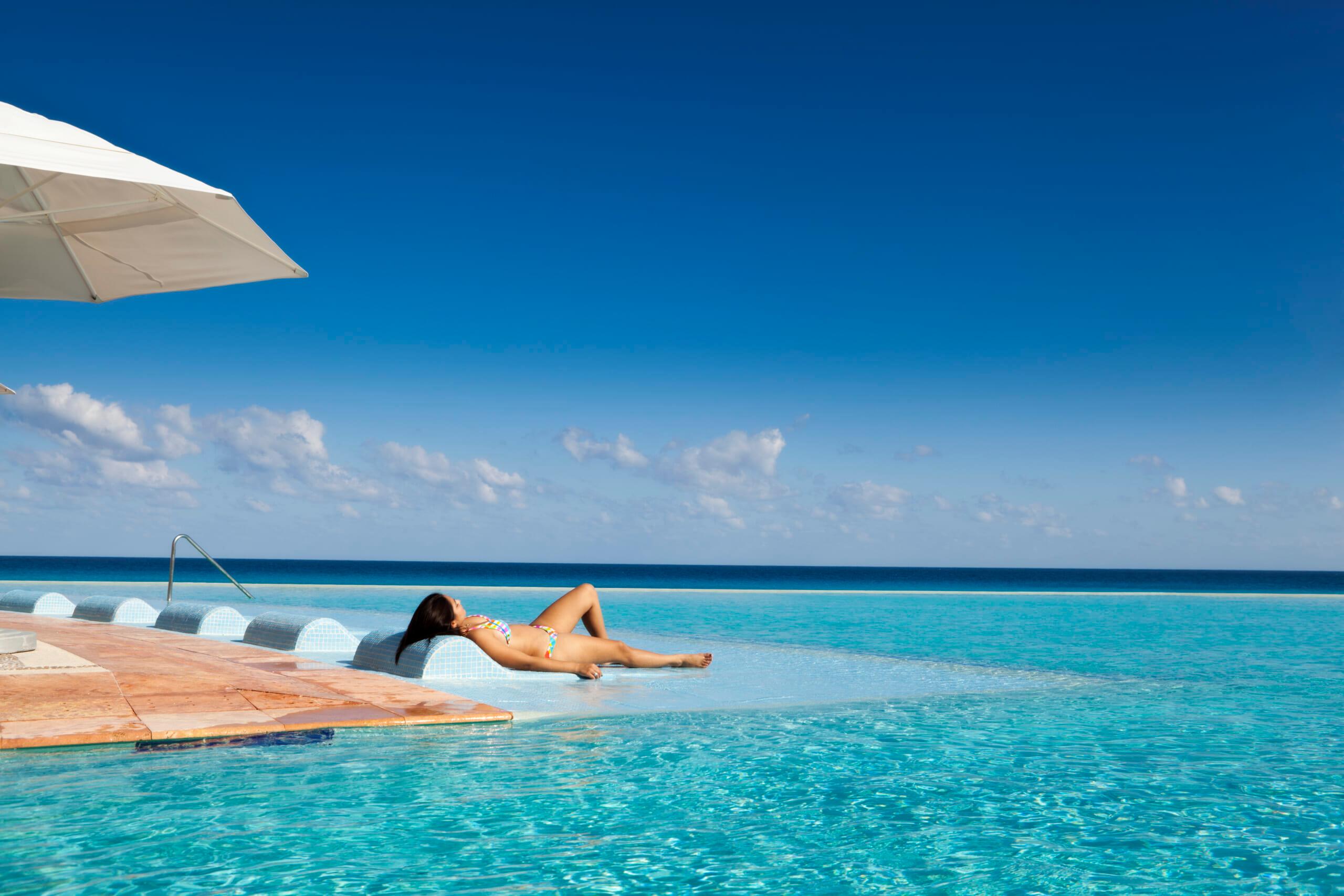 GettyImages-184853918 A young woman by a tropical beach resort hotel infinity pool on the Caribbean Sea, Cancun, Riviera Maya, Mexico.