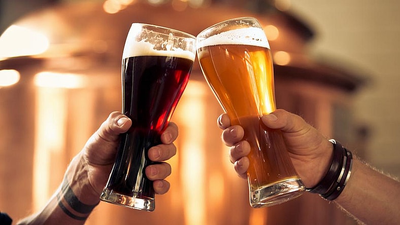 Image of hands toasting with glasses of craft beer in front of distillery vat.