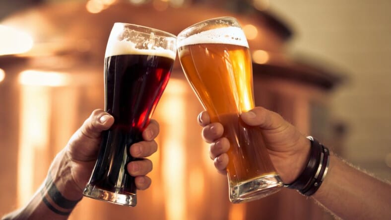 Image of hands toasting with glasses of craft beer in front of distillery vat.