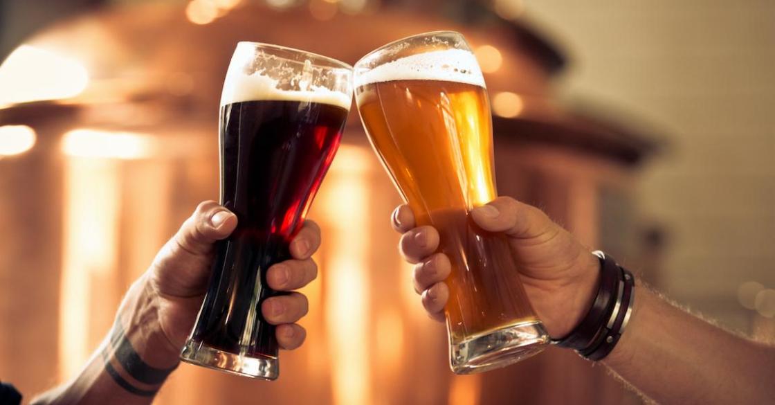Image of hands toasting with glasses of craft beer in front of distillery vat.