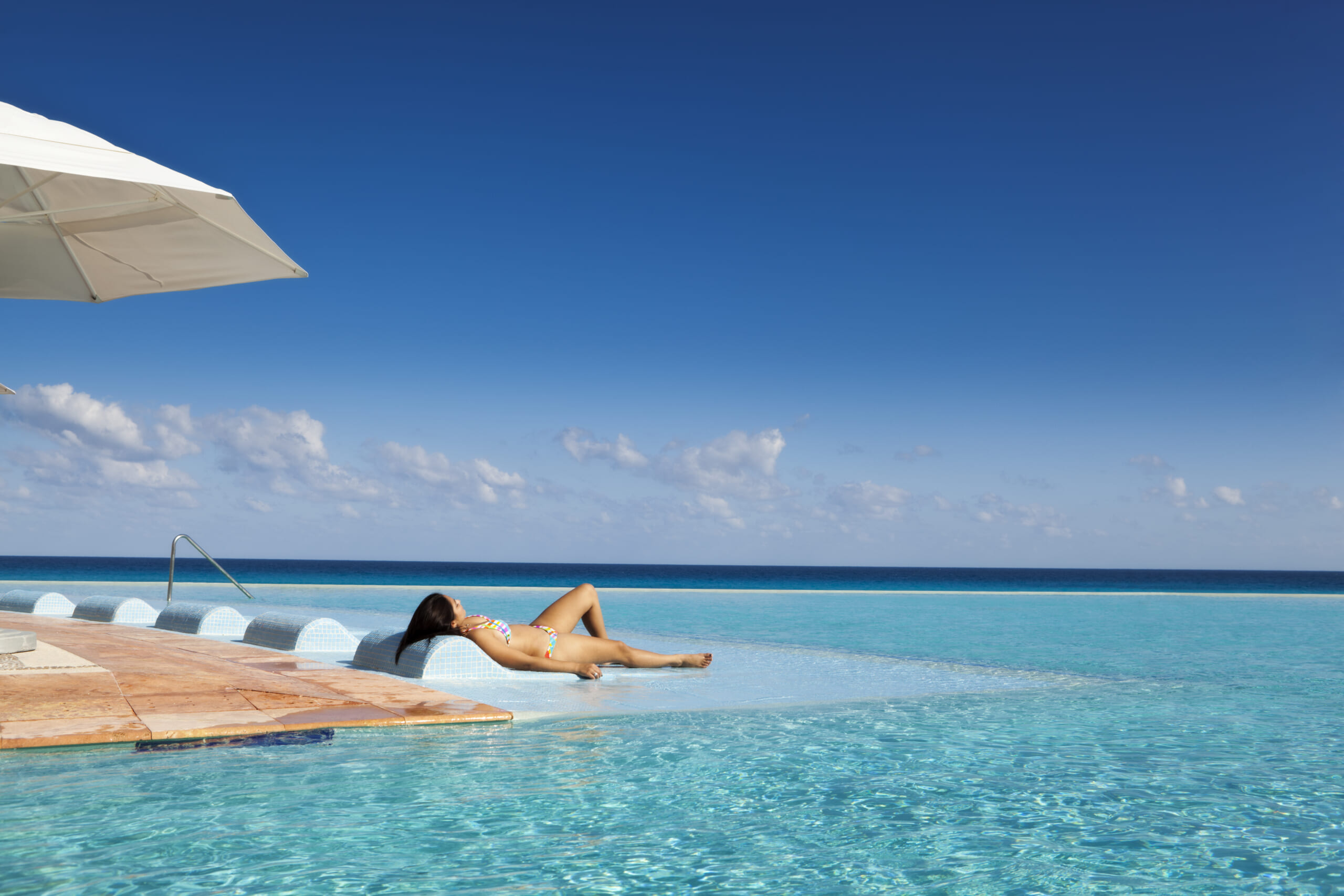 A young woman by a tropical beach resort hotel infinity pool on the Caribbean Sea, Cancun, Riviera Maya, Mexico.